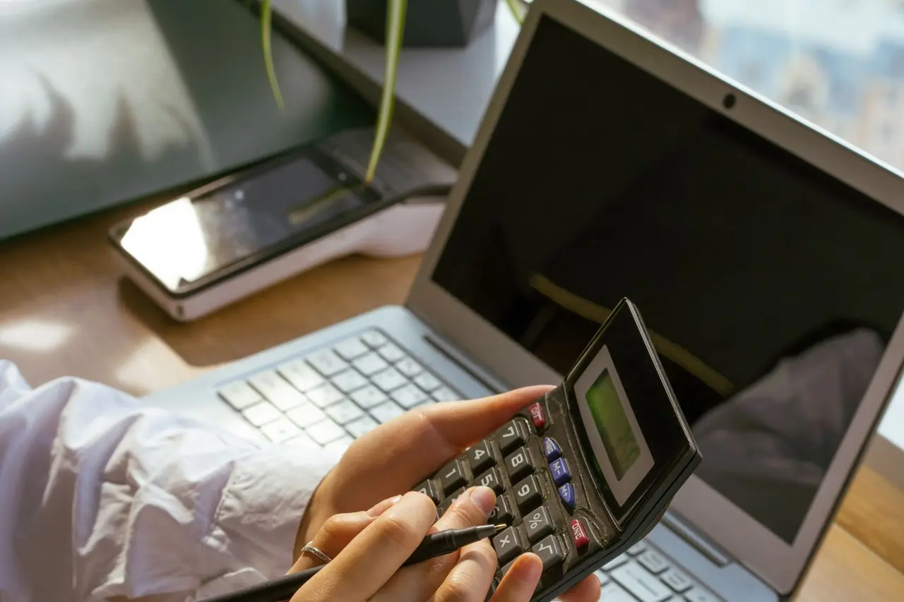 Person calculating costs beside a laptop and notebook
